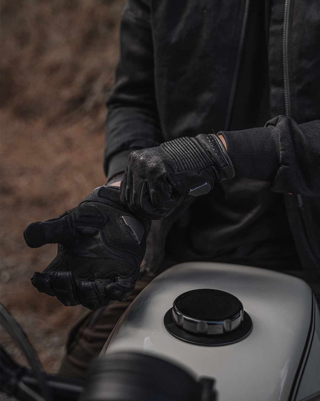 Black leather motorcycle gloves worn by rider, combining style, comfort, and advanced knuckle and palm protection features
