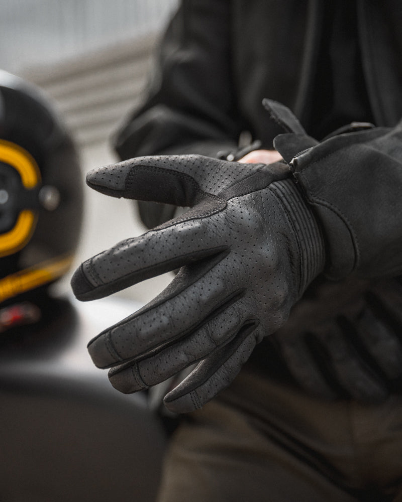 Rider wearing black motorcycle gloves with TPU knuckle guard and touchscreen-compatible fingertips, combining style, comfort, and protection for any ride