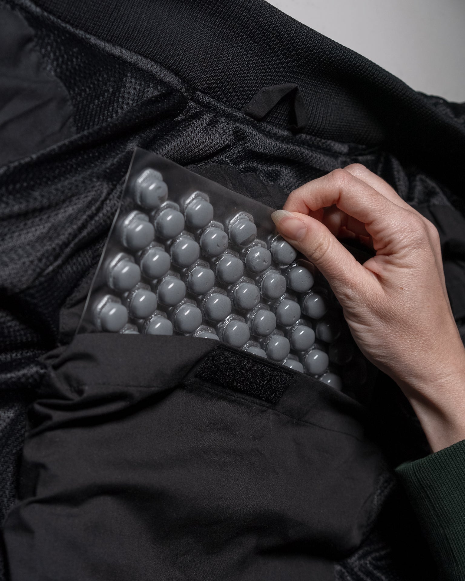Person inserting TPU-coated impact-absorbing polymer bubbles on stealth body armor sheet