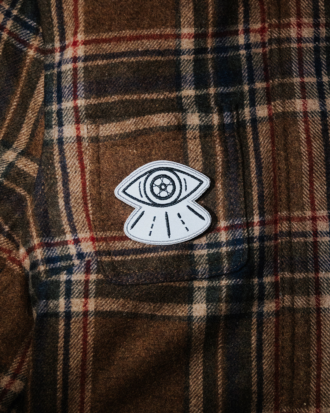 Reflective black and white motorcycle patch with eye design on brown flannel shirt